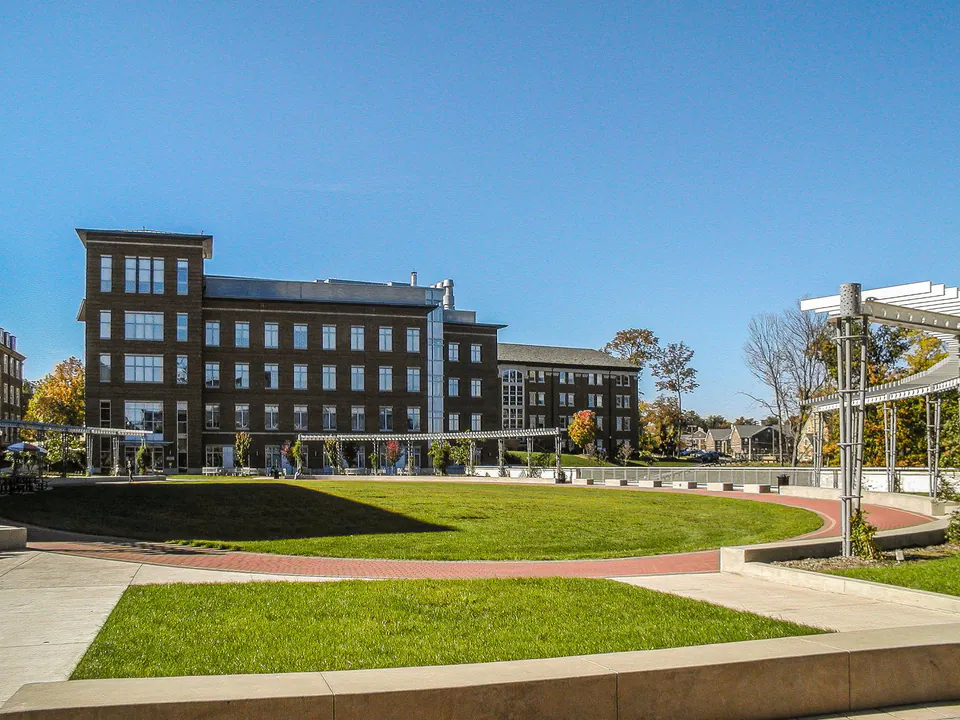 Campus courtyard with lawn panel, long brick walk, concrete seat wall, and brick academic buildings